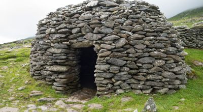 hC9xkIkA A stone beehive hut with a small entrance, seen on a Slea Head drive tour from Dingle.