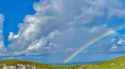 A rainbow arcs over green cliffs on a Wild Atlantic Way private tour Dingle, beneath blue skies.