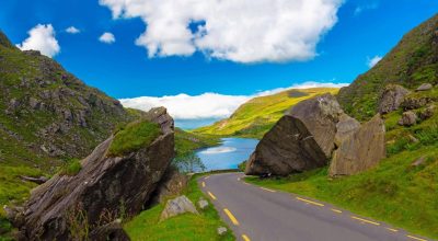 A winding road on the Slea Head drive tour from Dingle passes rocks in a green mountain landscape.