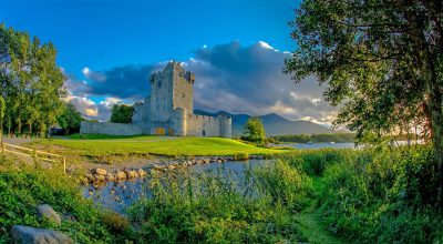 Stone castle ruins by a lake on the Slea Head drive tour from Dingle, with mountains and trees.