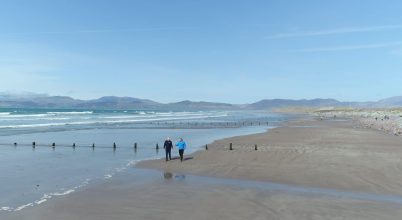Two people stroll a sandy beach with mountains, on a Dingle Peninsula private day tour.
