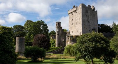 Stone castle with round towers seen on a Slea Head drive tour from Dingle, amidst trees and grass.