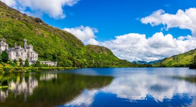 Castle by a lakeshore, seen on a Wild Atlantic Way private tour Dingle, calm water reflects blue sky.